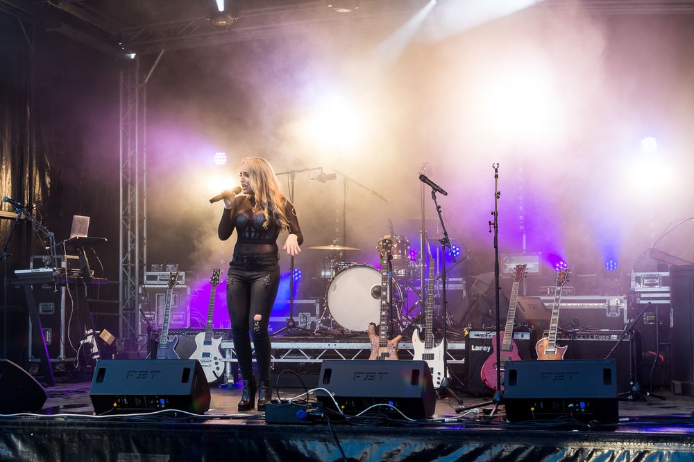 Concert performers on stage with bright illuminated lights and fog effects creating a dramatic atmosphere during a live show.