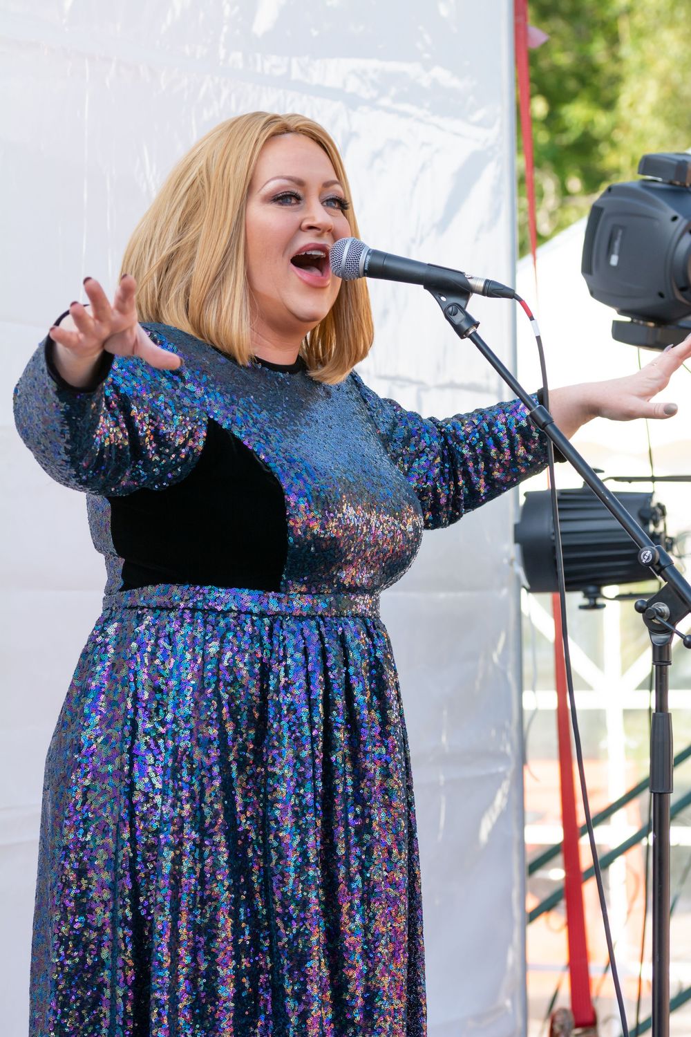 Singer in sparkly blue sequined gown performs on stage with microphone in dramatic pose.