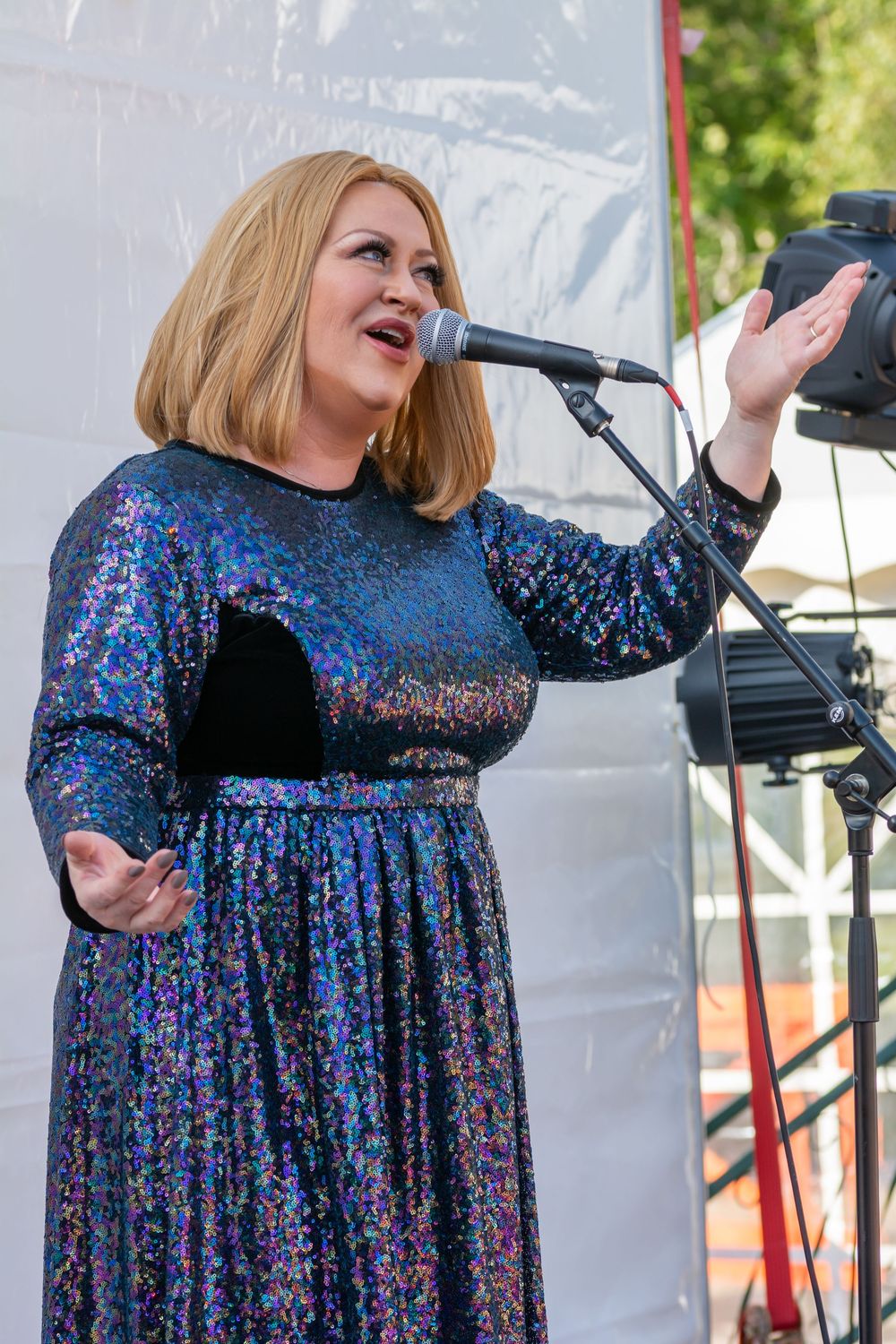 Performer in sparkly blue dress sings passionately on outdoor stage through sequence of expressive moments.