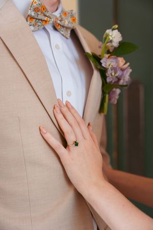 Close-up sequence showing hands gently touching a beige suit lapel with delicate floral boutonniere pinned to it.