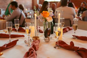 A wedding reception table setting with lit candles, floral centerpieces, and champagne glasses near burgundy napkins.