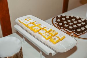 Small yellow lemon tartlets arranged in a row on a white ceramic platter next to chocolate desserts.