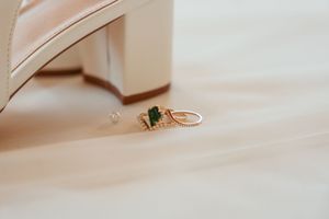 A delicate gold ring with an emerald-cut green gemstone sits on a soft pink fabric background.