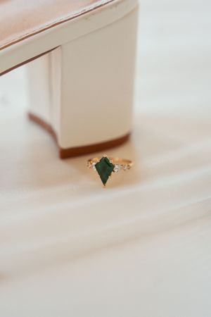 Delicate gold ring featuring an emerald-cut green gemstone with small accent diamonds on a soft cream background.