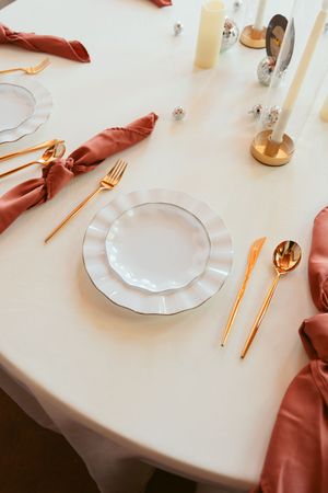 Elegant table setting with rose gold cutlery, white plates, and coral napkins on crisp white tablecloth.