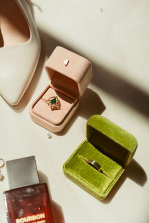Multiple small jewelry ring boxes in pink, green, and burgundy velvet textures cast dramatic shadows on a white surface.