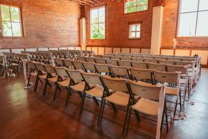 Rows of empty wooden folding chairs arranged in an auditorium with rustic wood paneled walls and natural lighting.