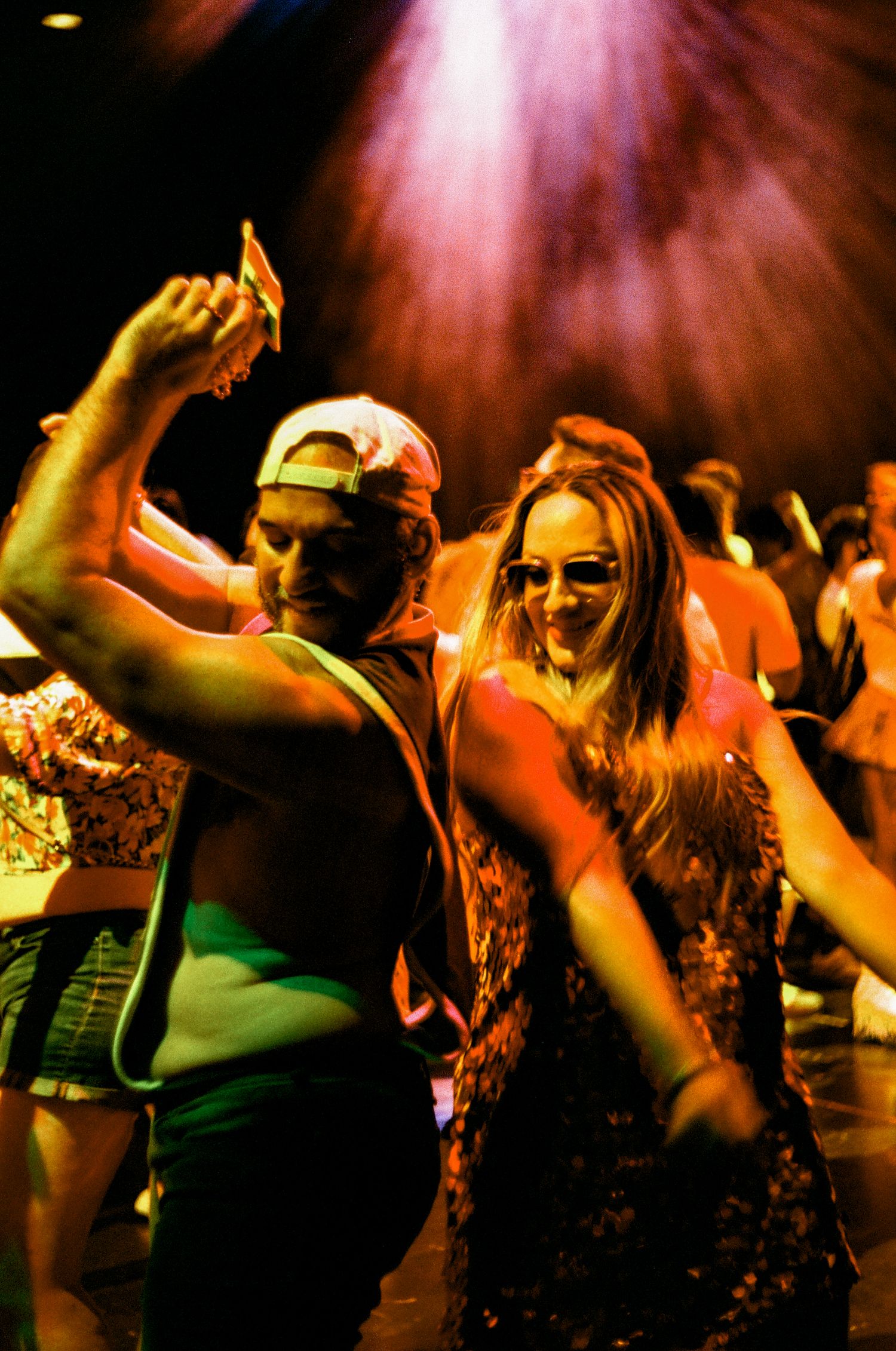 Enthusiastic partygoers dancing under dramatic pink stage lighting at a nightclub event.