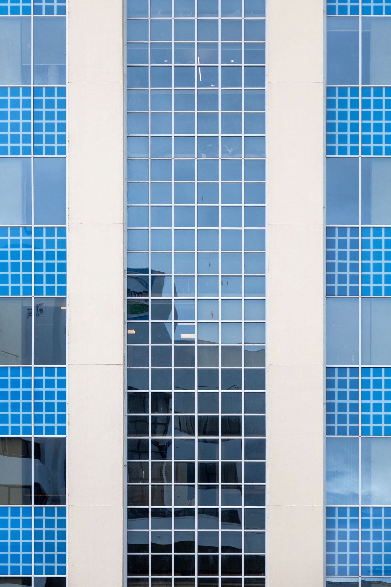 Grid of bright blue windows against a cream facade, forming a retro digital-style architectural composition.