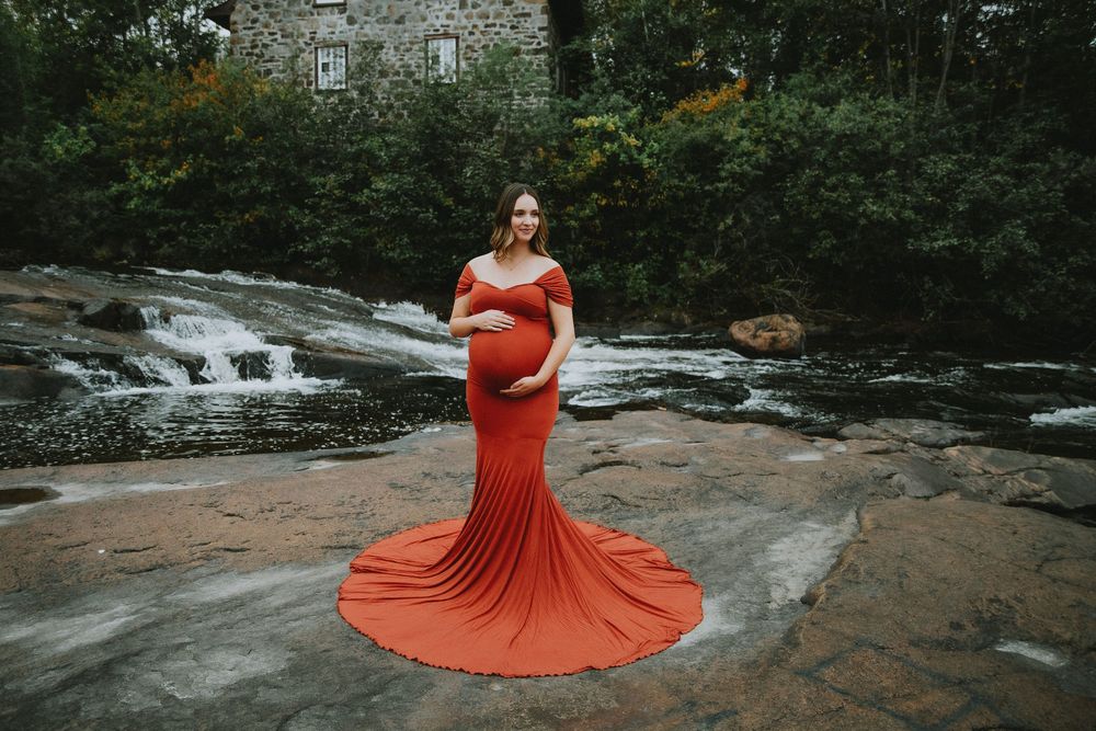 A maternity photo featuring a flowing red gown against a cascading waterfall backdrop.