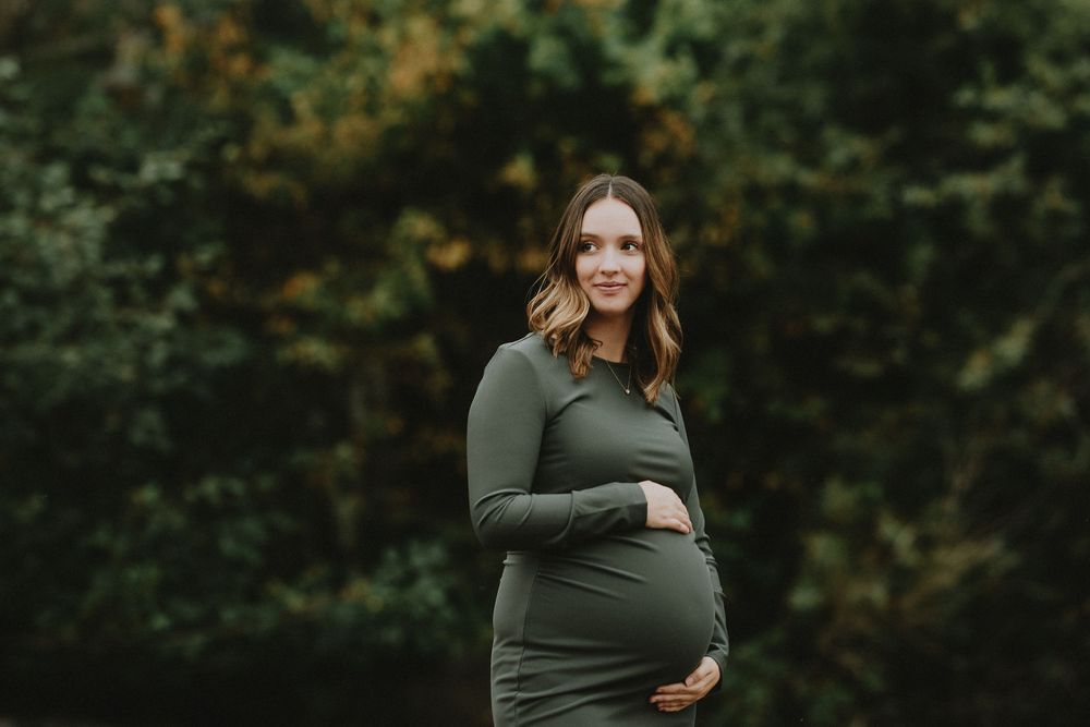 A maternity photoshoot in a green dress against a blurred forest background.