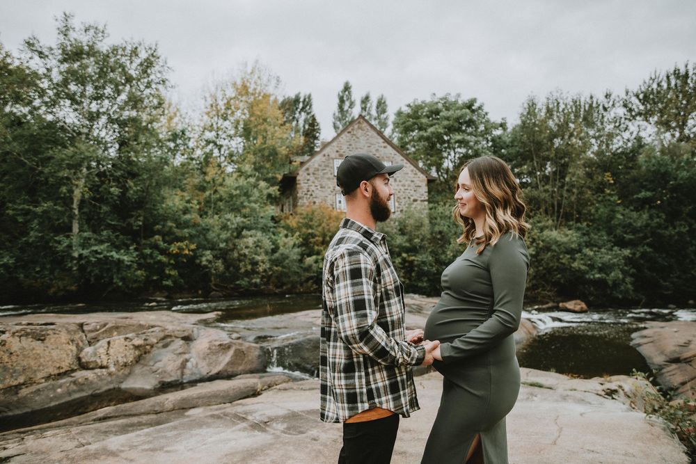 A couple embracing during maternity photoshoot on rocky terrain with stone building in background.