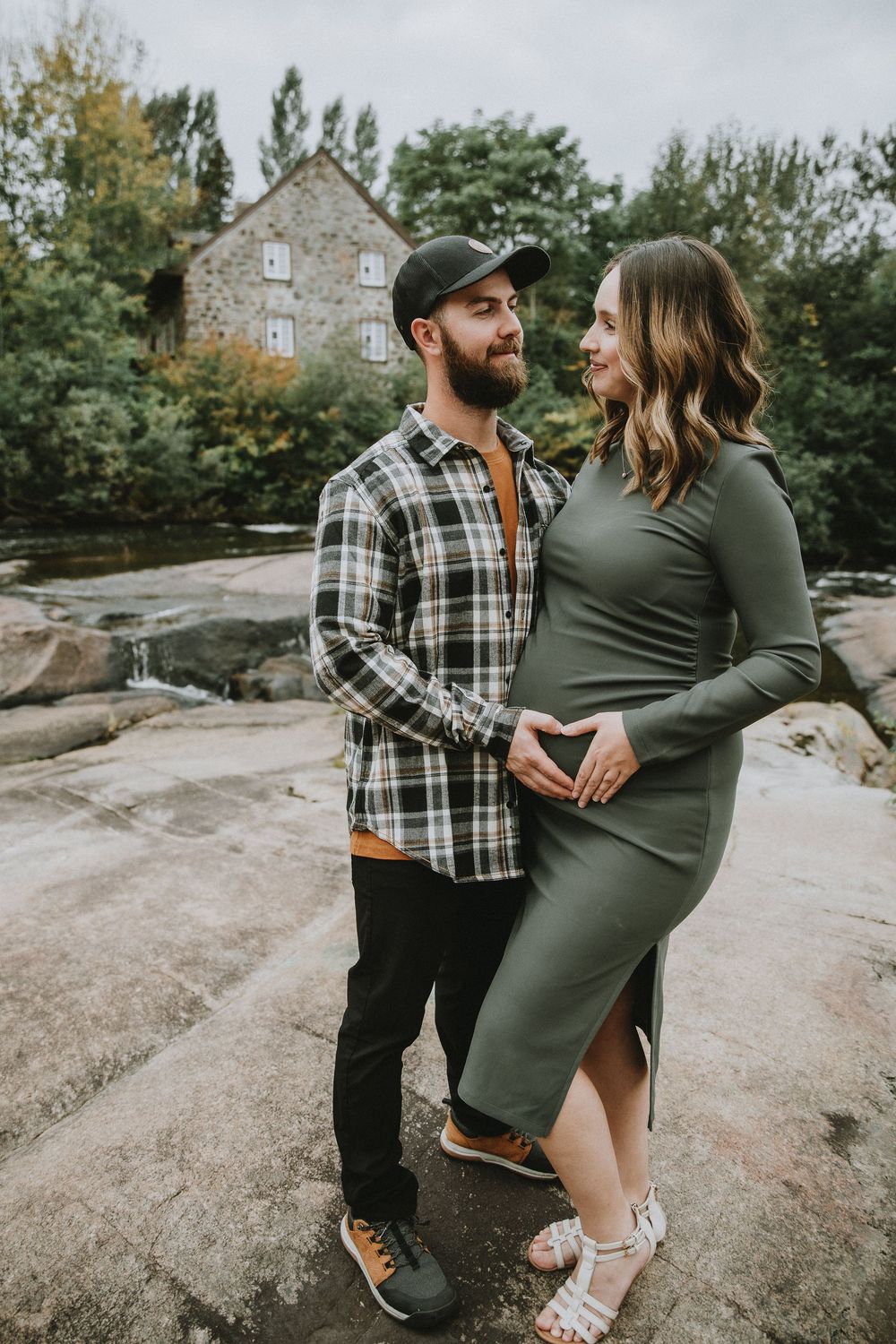 A romantic maternity portrait with couple on rocks near stone house.