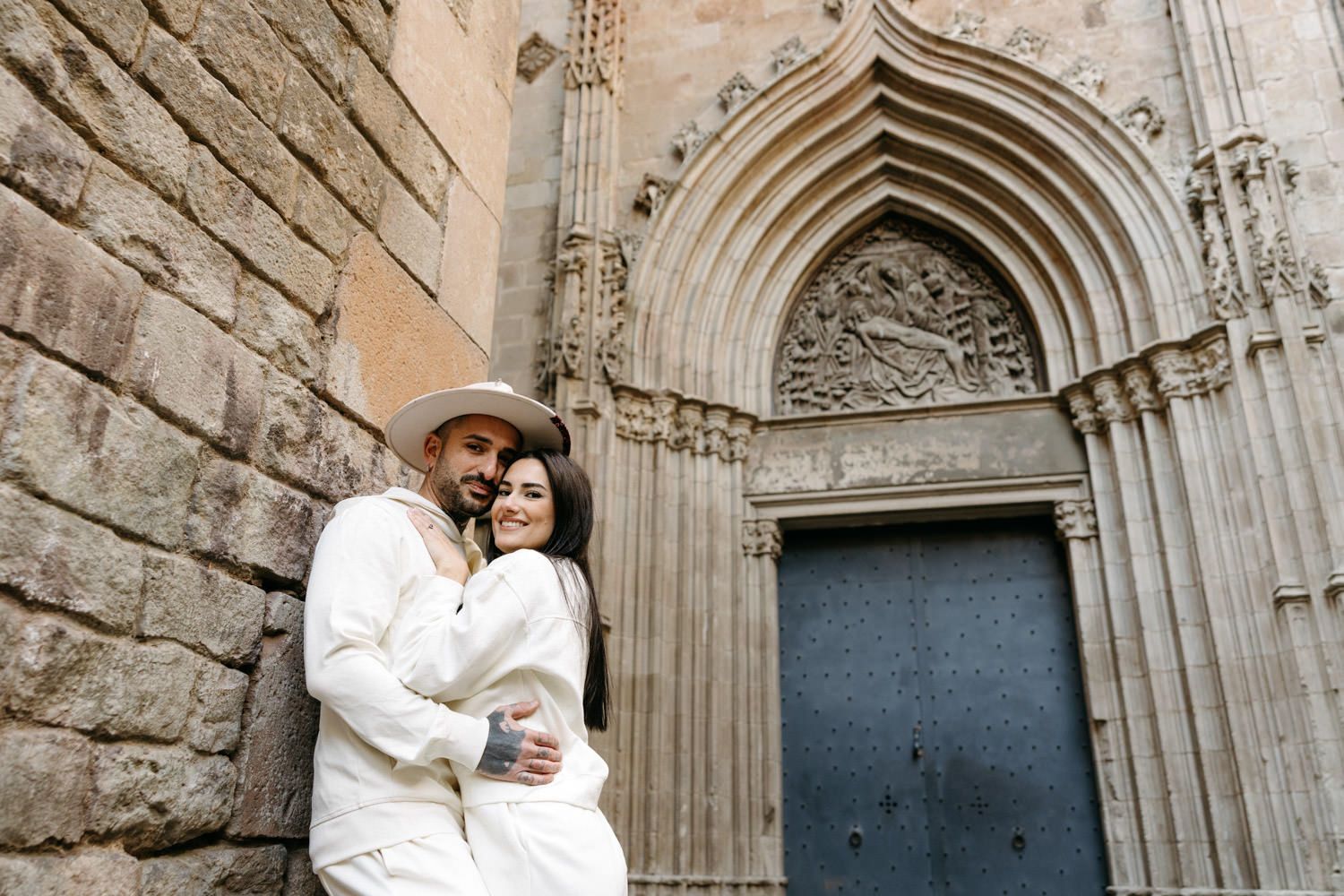 Couple embracing near ornate Gothic cathedral entrance with stone archways.