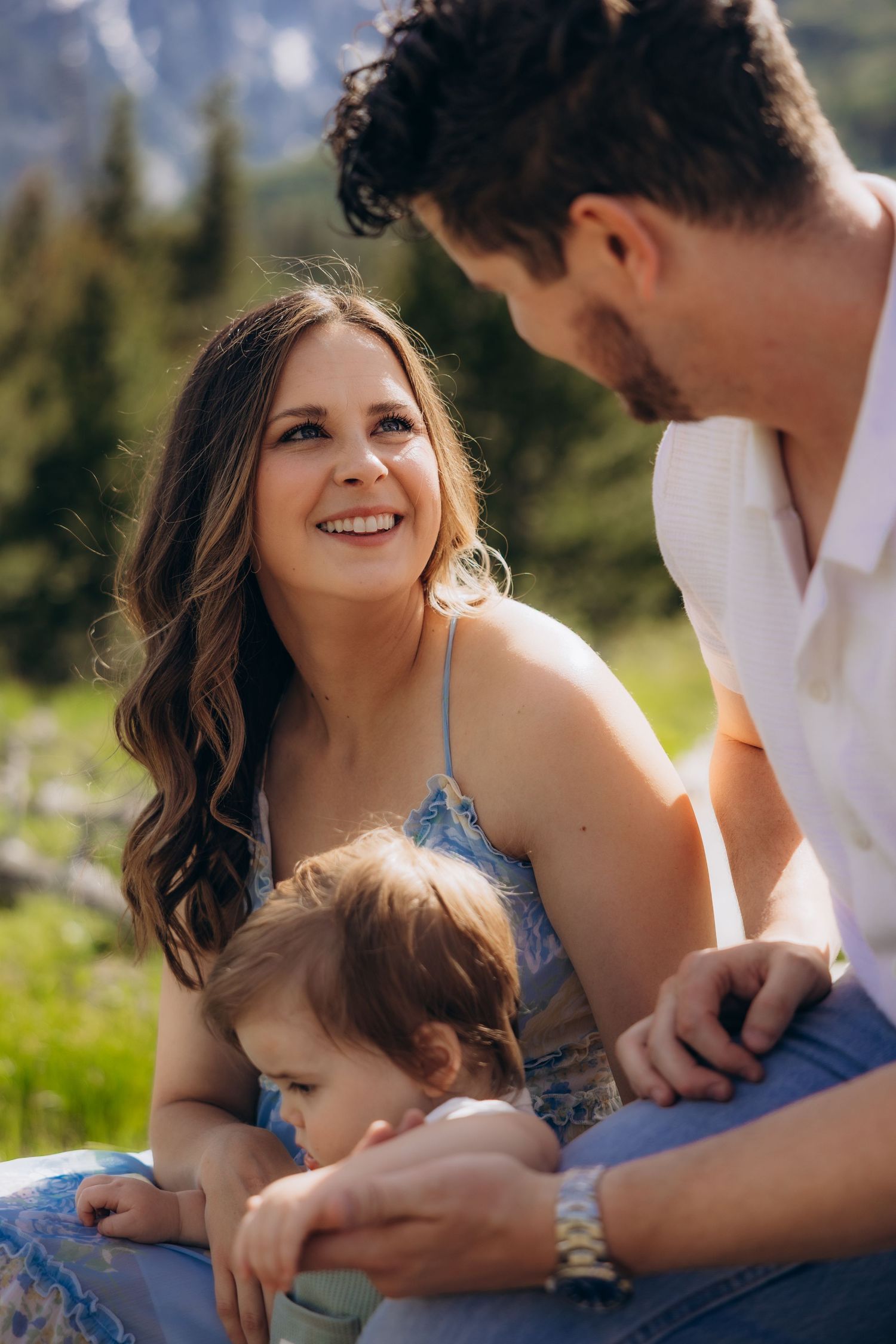 A couple spending time outdoors with their child on a sunny mountainside, sharing an intimate family moment together.