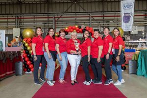 A group of people wearing matching red shirts pose together at an event with gold balloons in the background.