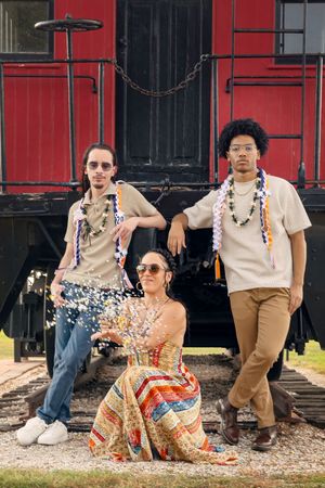 Five stylish individuals in vintage-inspired outfits pose casually against a red train car backdrop.