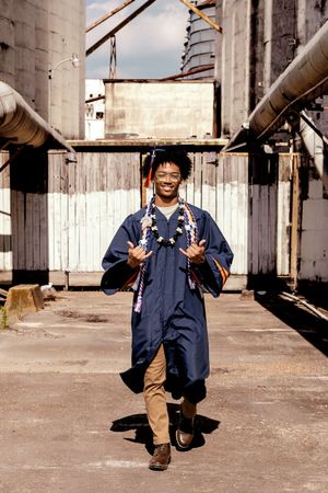 Person wearing navy workwear overalls and boots stands confidently in an industrial setting with pipes and metal structures.