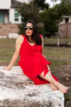 A figure in a vibrant red dress poses elegantly on a white stone surface outdoors.