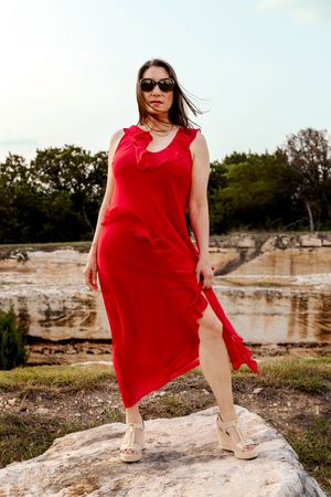 A person in a flowing red dress poses gracefully on rocky terrain during golden hour.