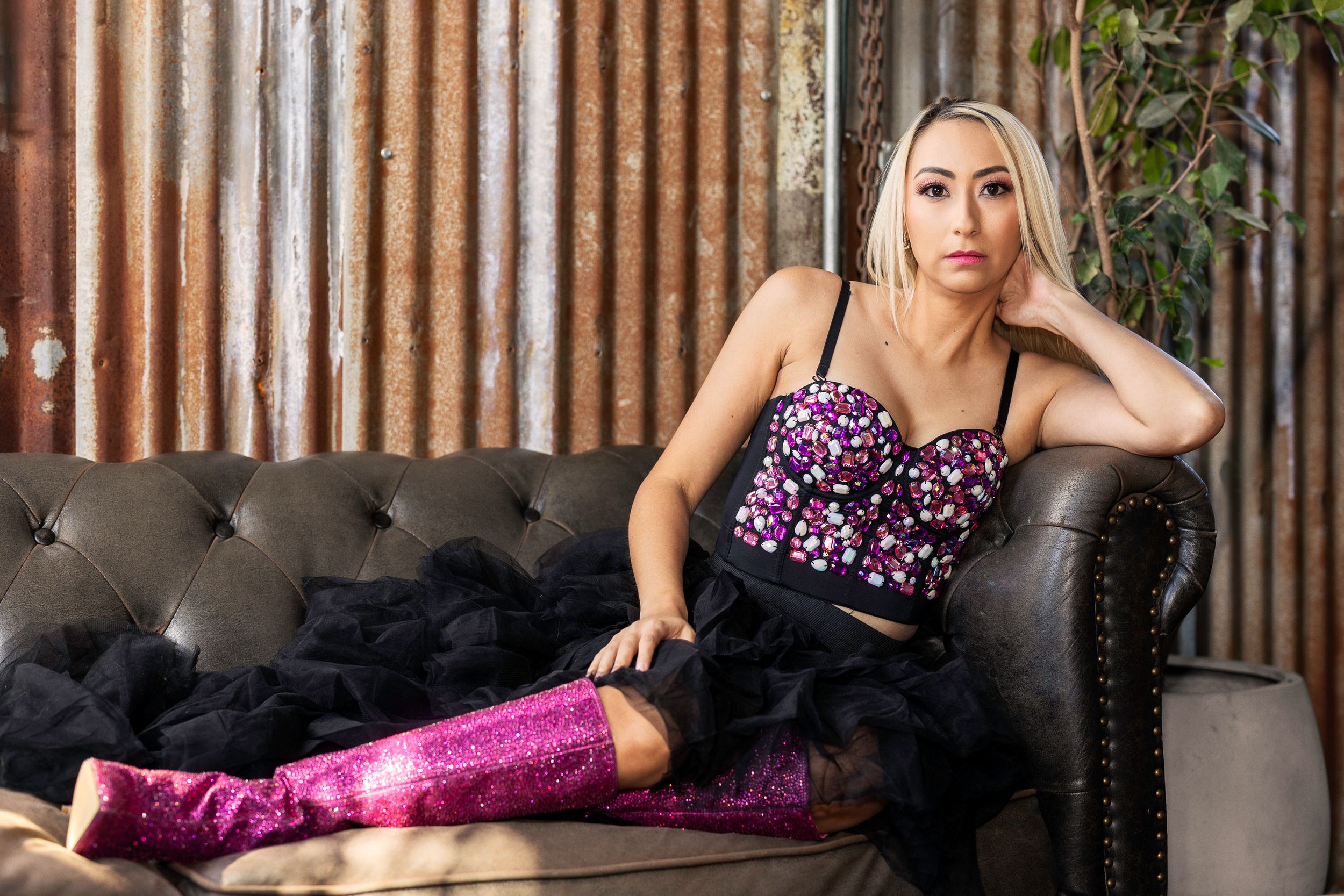 A glamorous lounging pose on a tufted leather couch wearing a sparkly corset top and metallic pink pants.