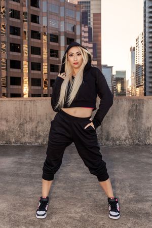 Person in black crop top and baggy pants strikes dynamic poses against urban rooftop backdrop with city buildings.