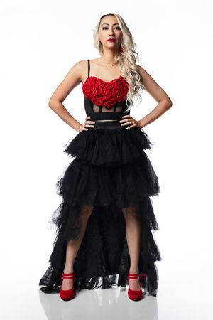Woman in red rose bustier top, black tiered tulle skirt, and red heels posing confidently on white background.