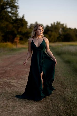 Person wearing a flowing black dress poses gracefully in an outdoor field at sunset.