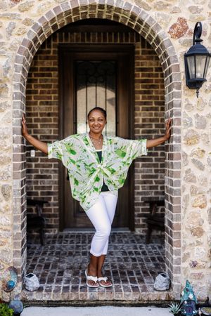 Standing in a stone archway entrance, someone poses wearing a green floral print top with white capri pants.