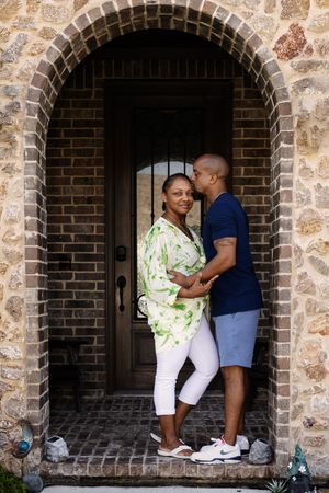 A couple embraces in a romantic moment under a stone archway at sunset.
