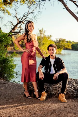 Stylish couple poses together by a lake at sunset with yellow leaves and trees in the background.