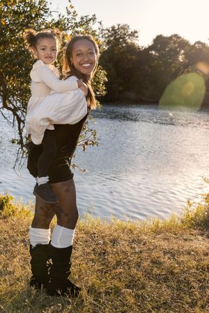 A joyful moment captured at sunset by a lake as two people share laughter and embrace in warm golden light.