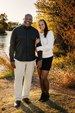 Couple shares tender moments at sunset by a lake with golden autumn foliage in the background.