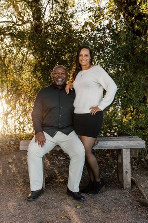 Couple sits together on wooden bench during golden hour photoshoot in natural outdoor setting.