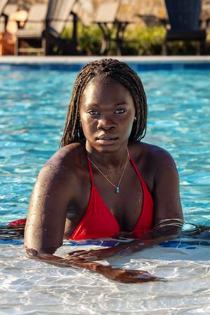 Someone relaxing at the edge of a swimming pool wearing a red swimsuit on a sunny day.