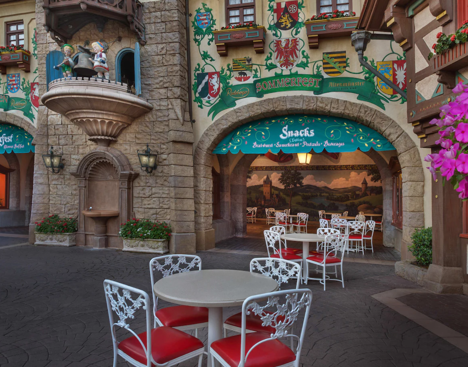 Outdoor cafe seating area with decorative stone archways and colorful flower displays.