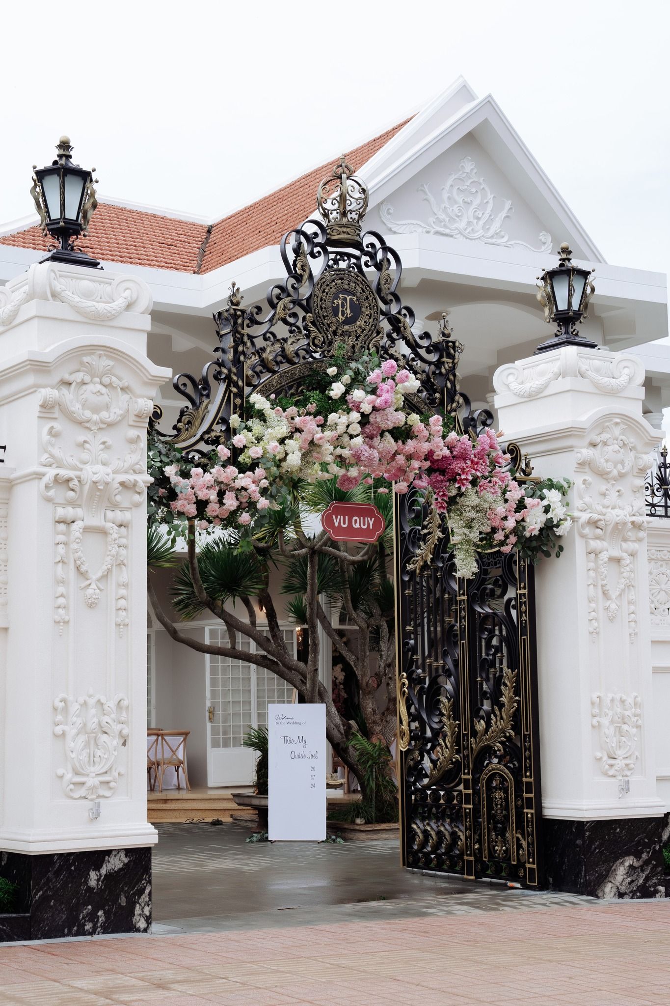 Ornate white wedding venue gate adorned with pink and white floral arrangements and iron details.
