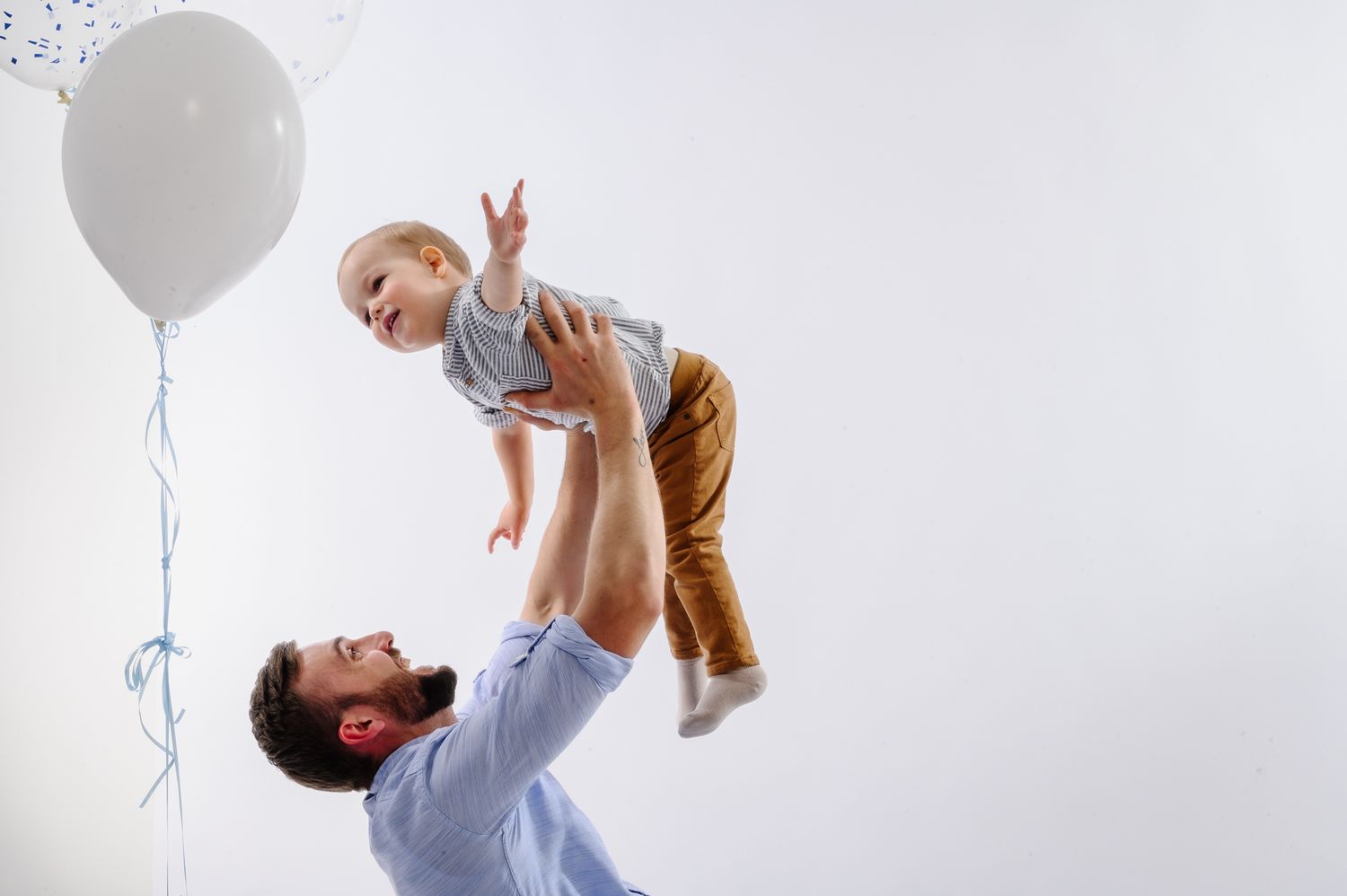 Playful father and baby portraits with white balloon against light background.