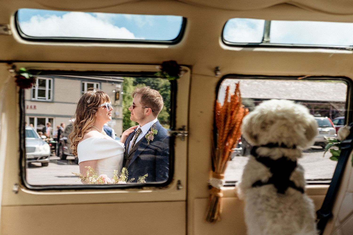 A couple sharing a romantic moment viewed through a vintage car window with a white dog in the foreground.