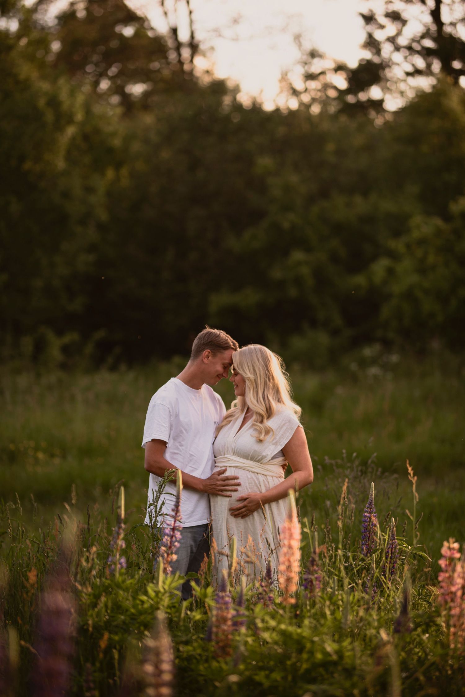 A romantic couple embraces in a wildflower meadow at sunset with pink lupines blooming in the foreground.
