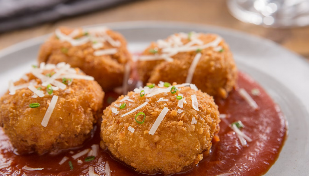 Golden fried arancini balls topped with cheese and marinara sauce on a white plate.