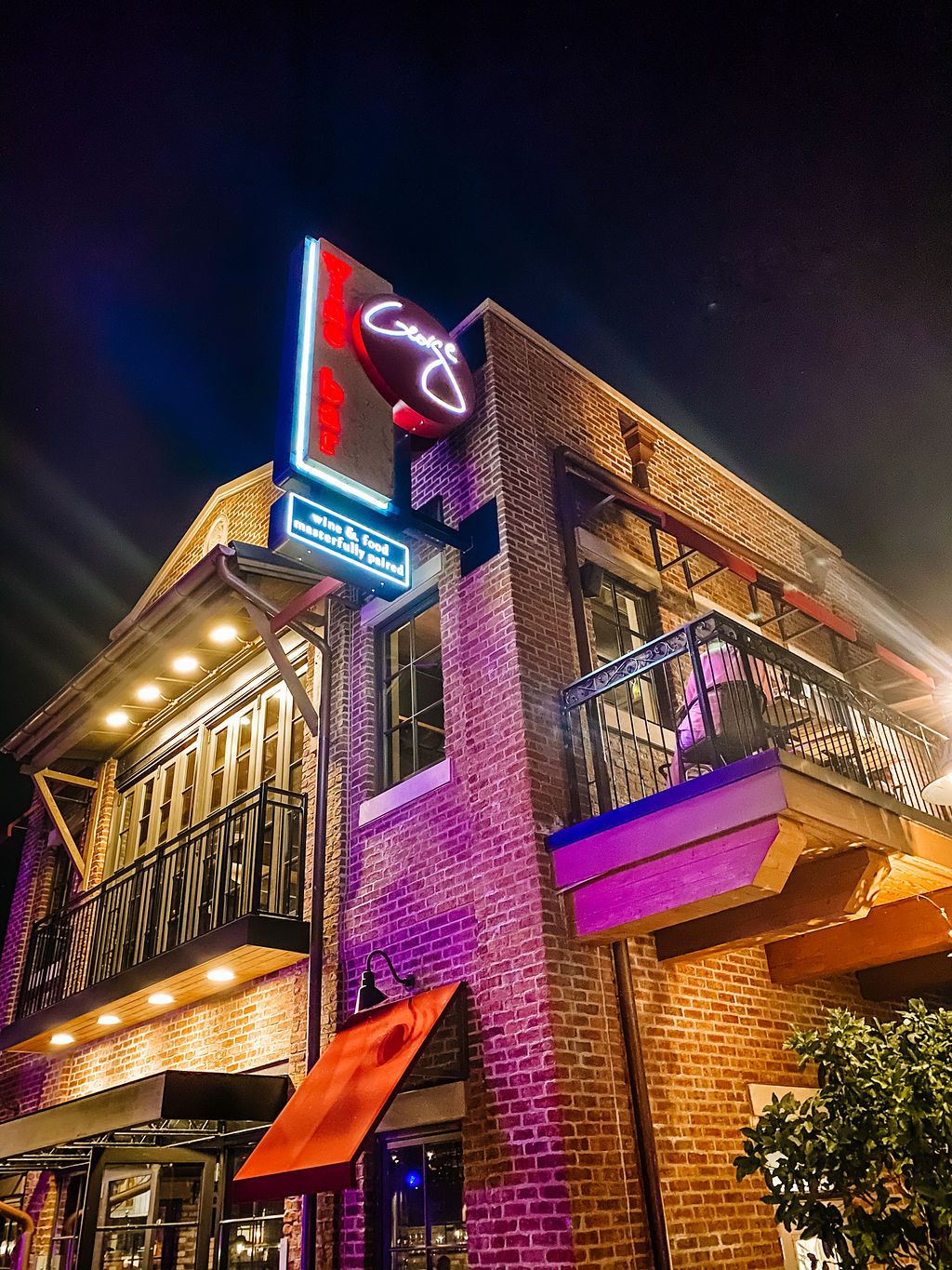 Brick restaurant exterior with neon signage and purple lighting at night.