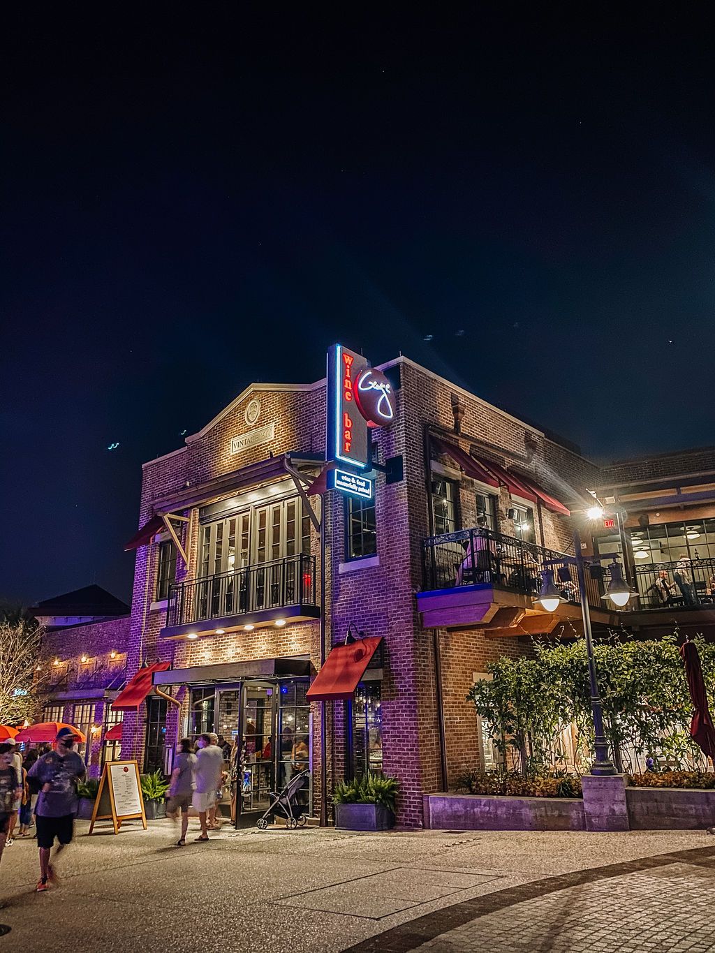 Two-story brick restaurant building illuminated with purple lights and neon signage at night.