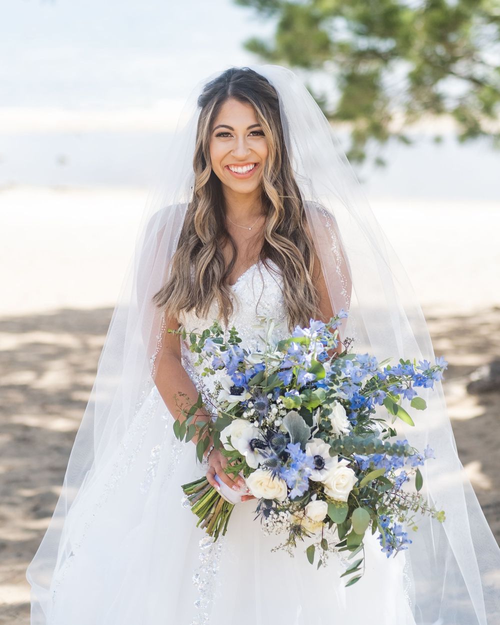 Beautiful bridal bouquet with blue delphinium, white roses and greenery creates an elegant garden-inspired arrangement.
