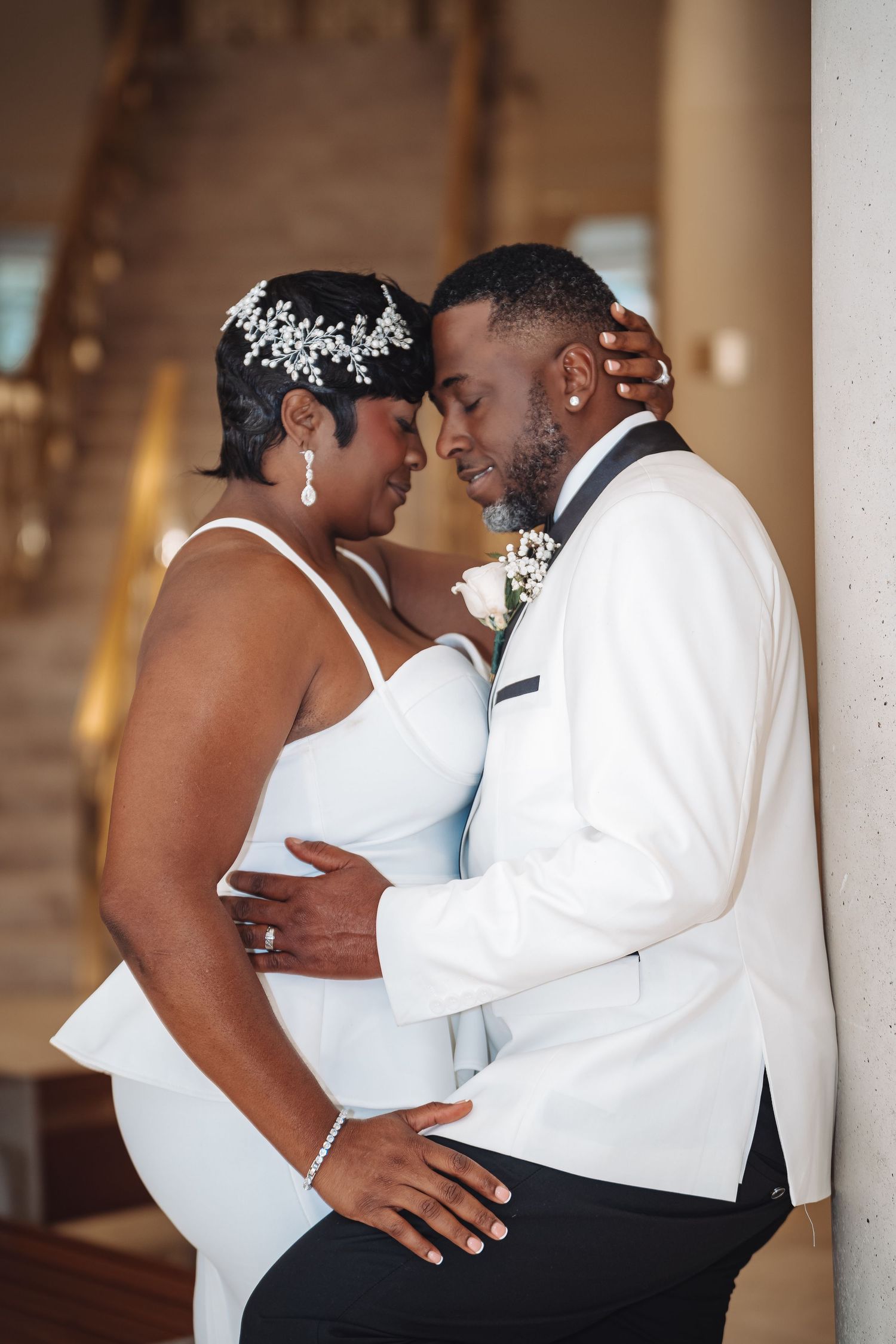 A tender wedding moment captured between a couple in matching white attire with the bride wearing a crystal hair accessory.