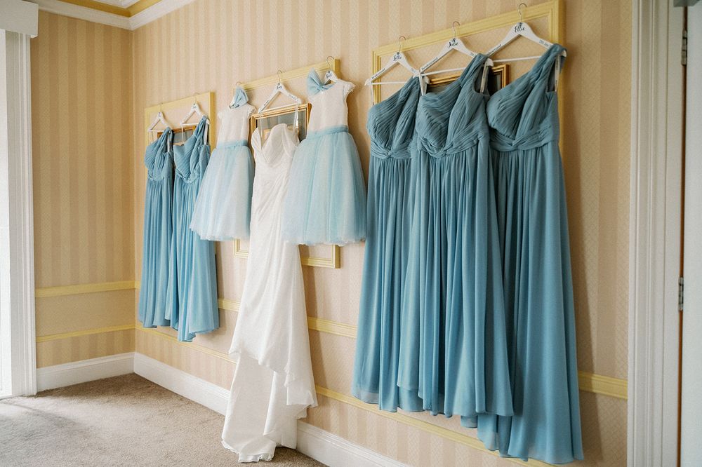 Light blue and white bridesmaid dresses hanging in a row against striped wallpaper.