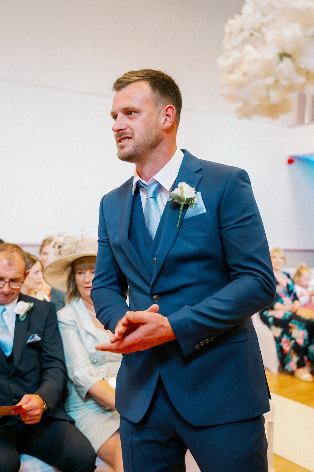 A groom in a navy blue suit and light blue tie during the wedding ceremony.