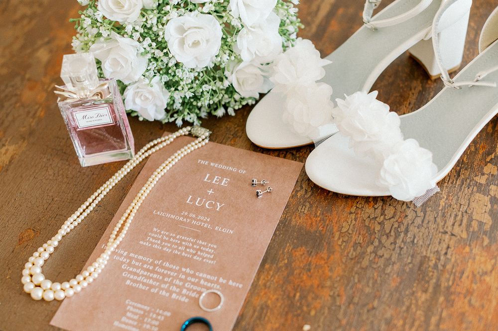 Wedding details including pearls, shoes, and invitations arranged on wooden surface.