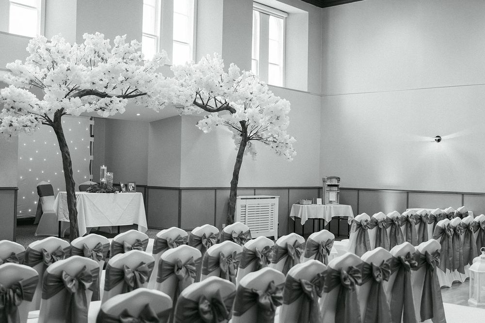 White cherry blossom trees line the aisle of an elegant indoor wedding ceremony space.