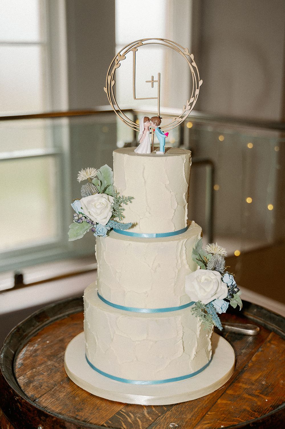 Three-tiered white wedding cake decorated with light blue ribbons and floral accents.
